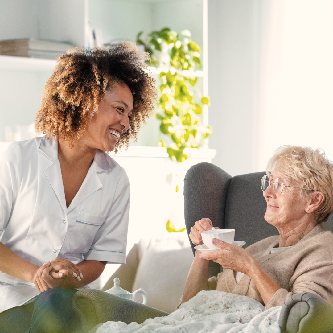 caregiver smiling with client who is seated drinking tea